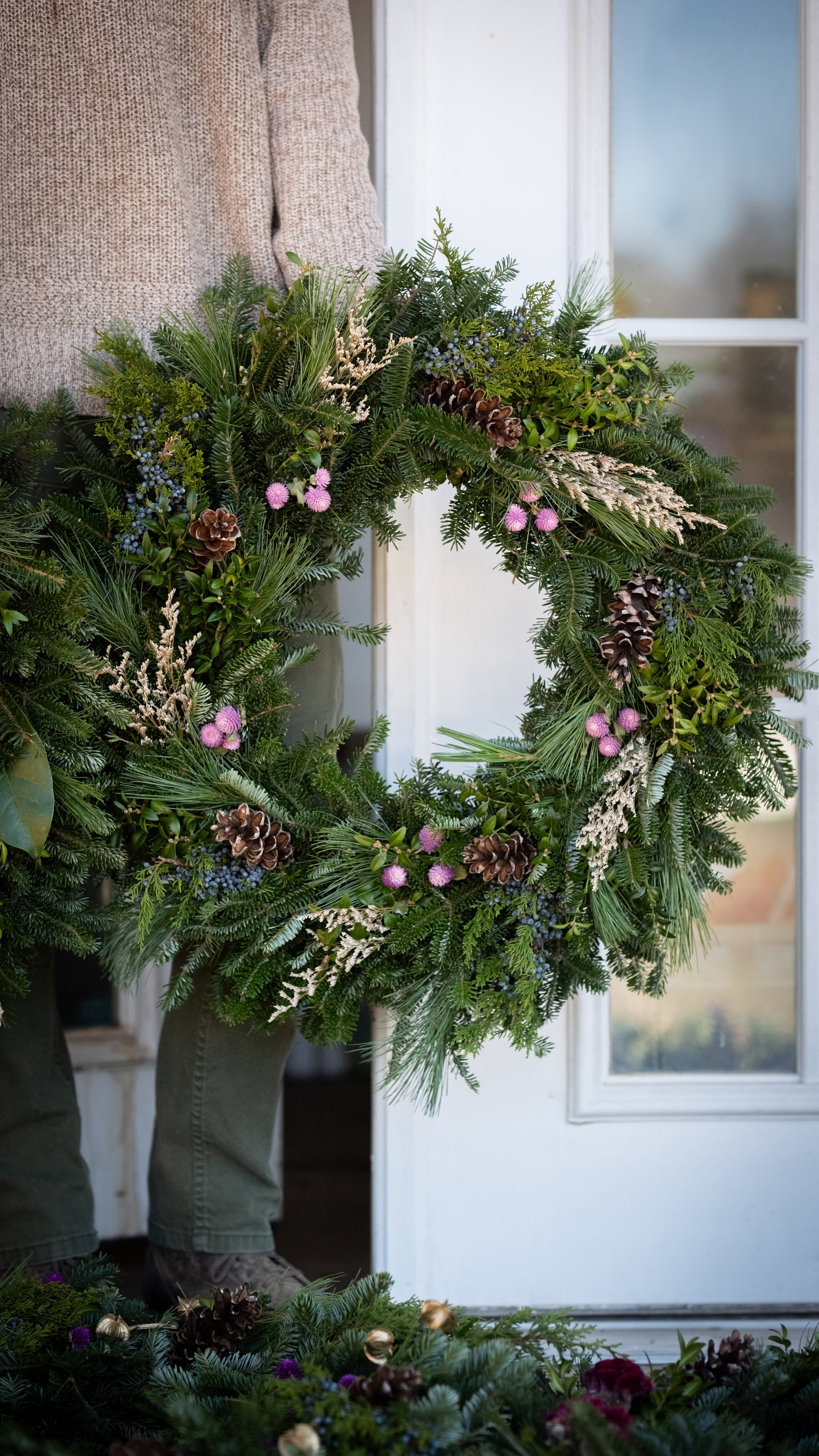 Green wreath with pinecones and pink flowers on a door