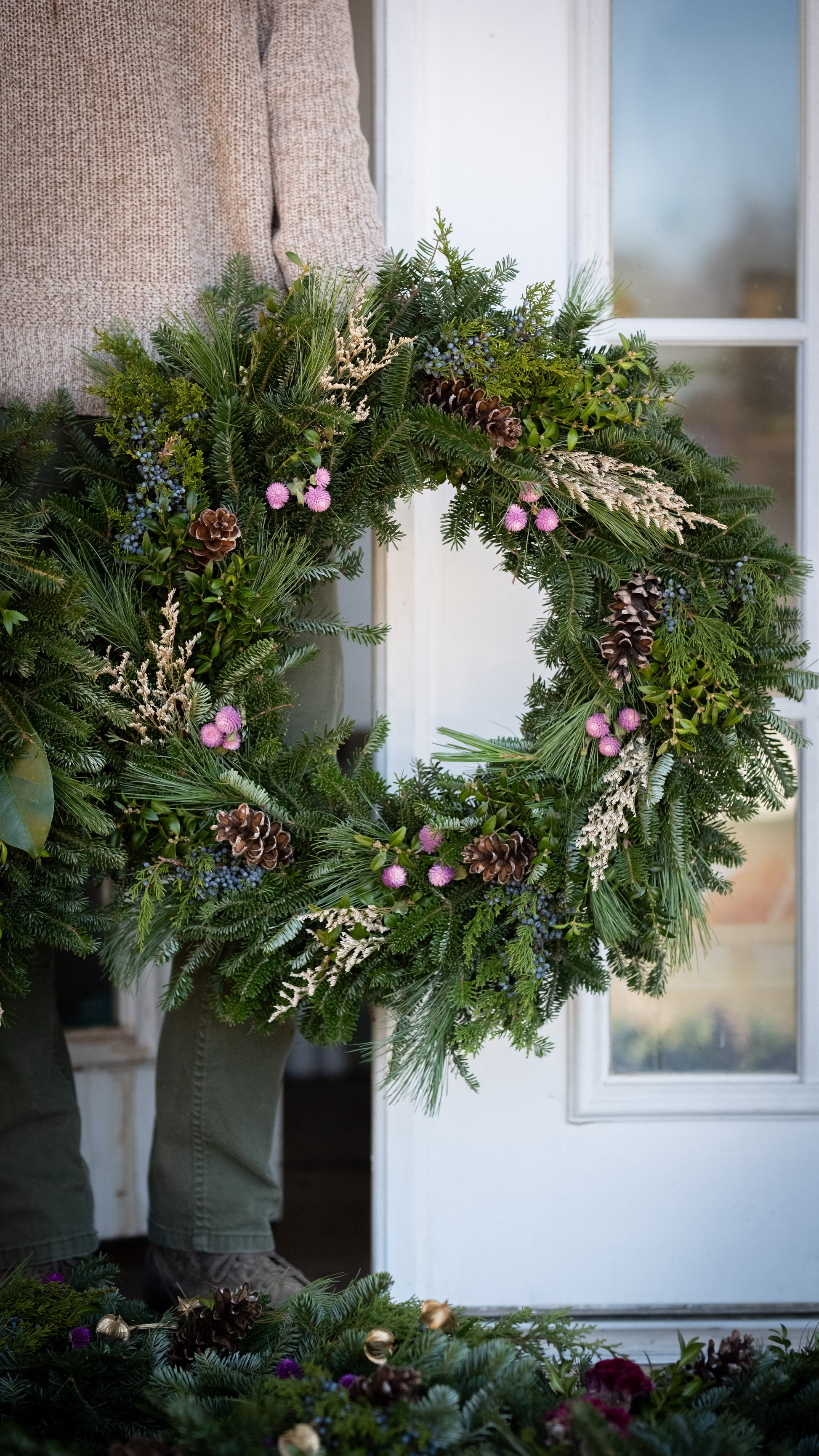 Green wreath with pinecones and pink flowers on a door