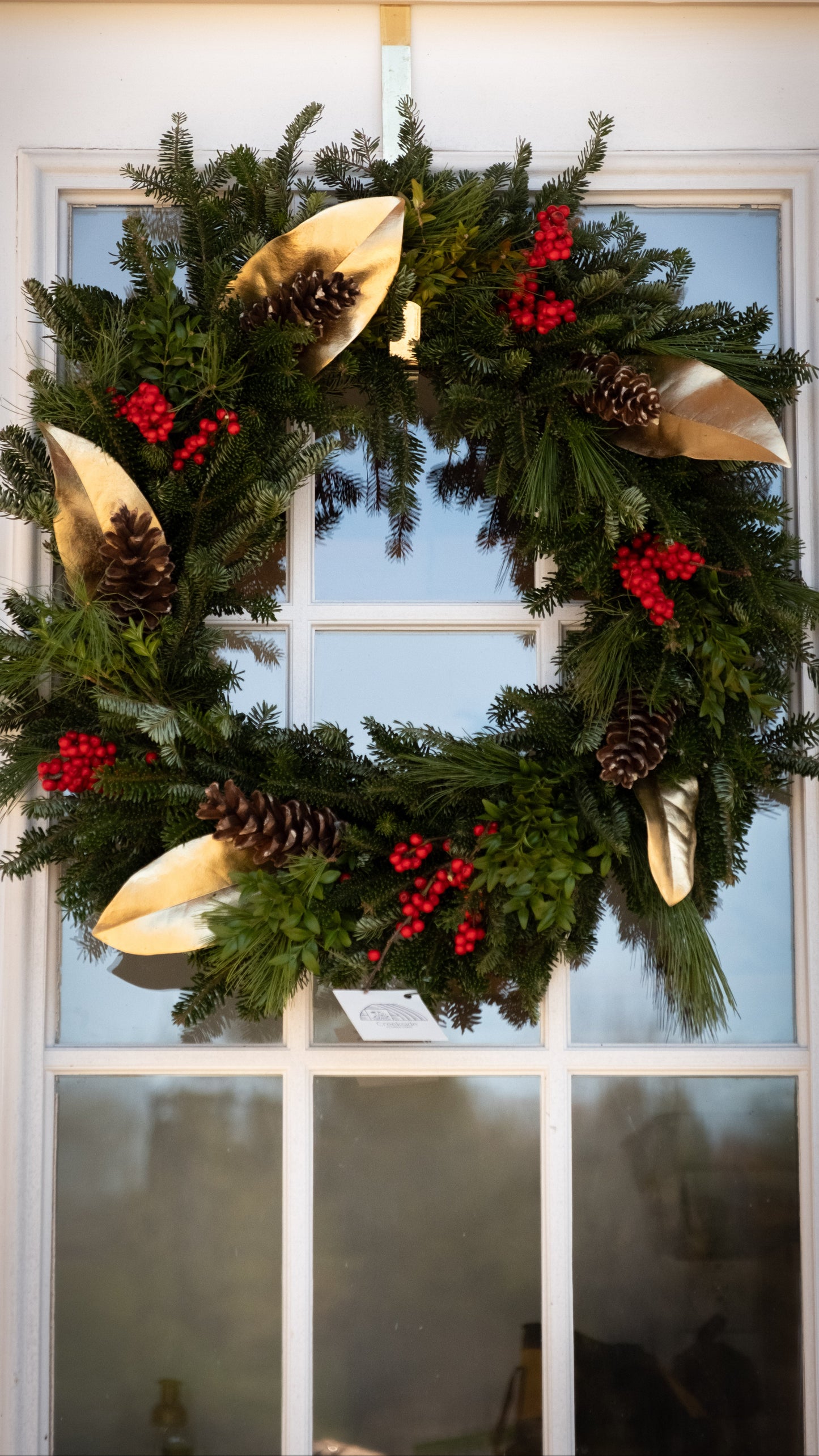 Christmas wreath with gold leaves, pine cones, and red berries on a front door.